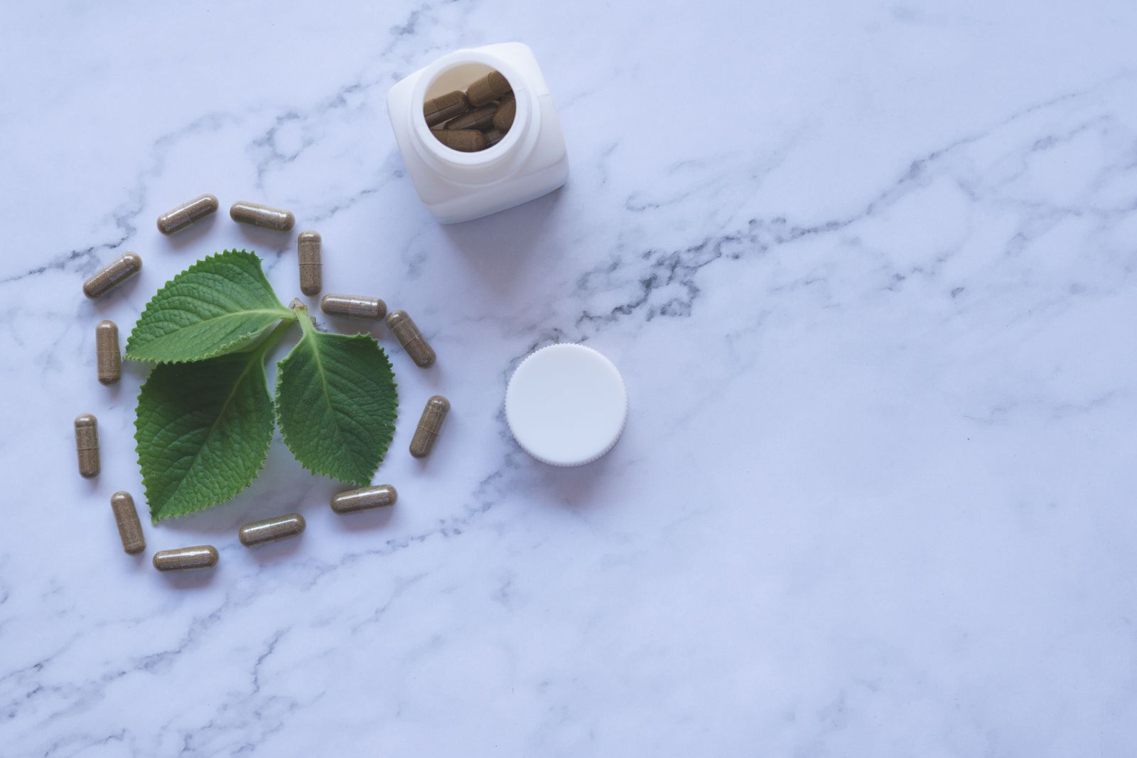 Kratom leaf beside herbal capsules